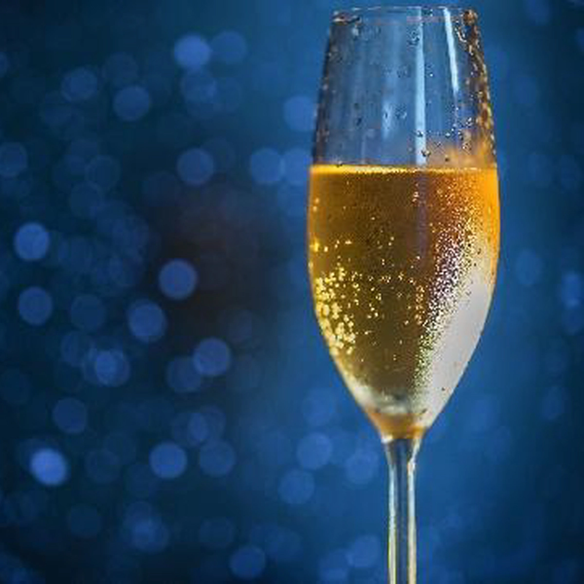 A gold champagne filled glass in front of a dark blue background